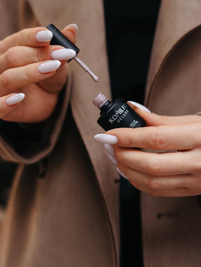 Close-up of a woman applying nude nail polish to her nails.